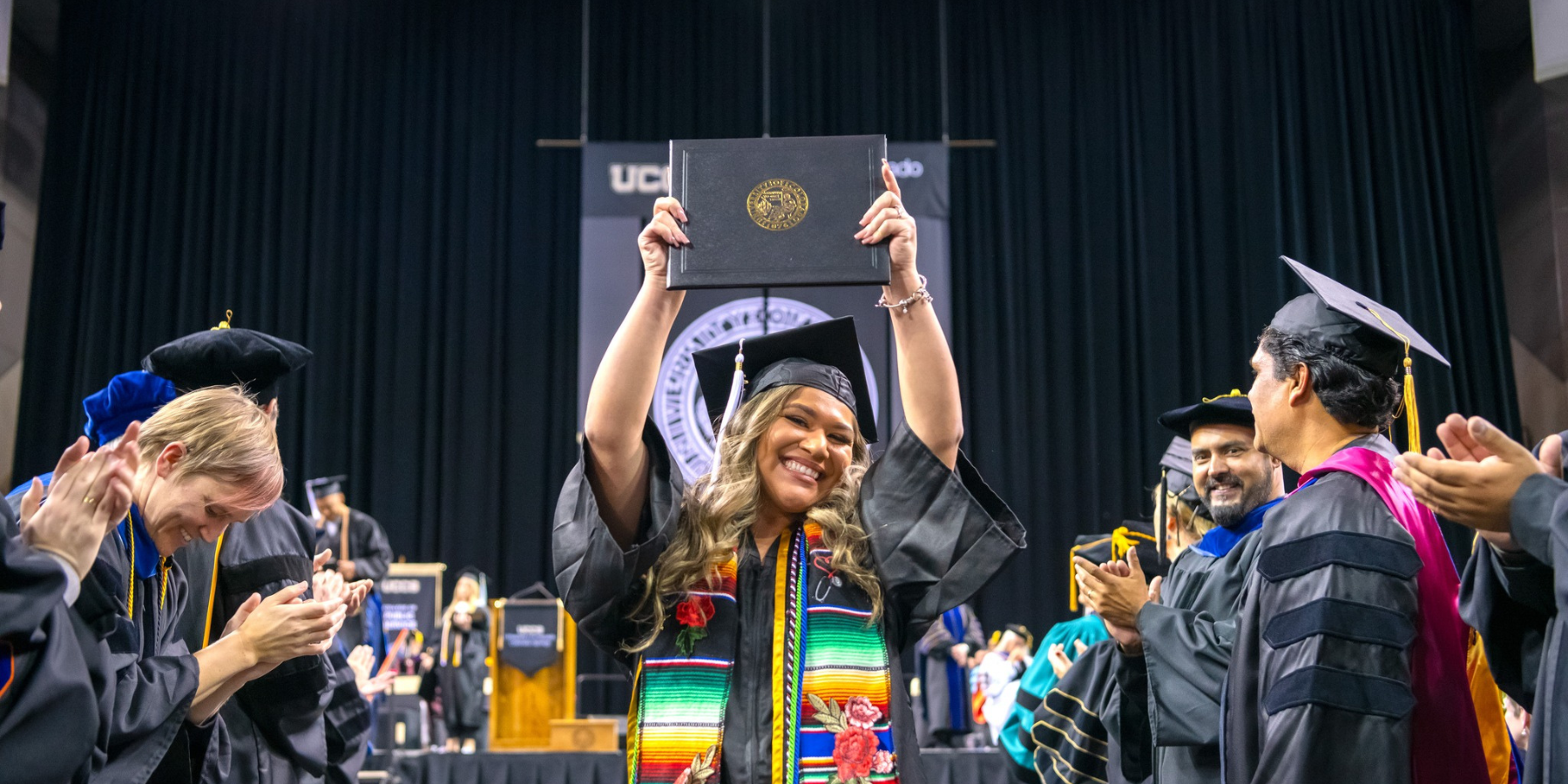 Photo of a first-generation college graduate holding up their diploma cover at UCCS Commencement.